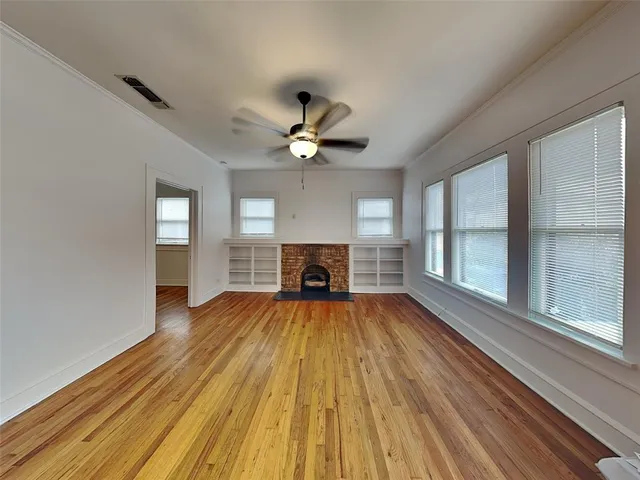 a view of an empty room with wooden floor fireplace and a window