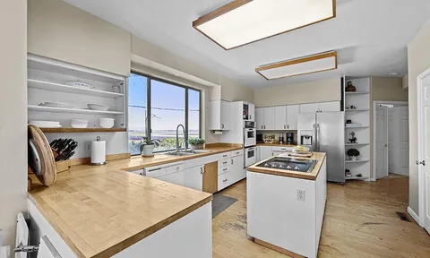 a kitchen with stainless steel appliances granite countertop a stove top oven a sink a refrigerator and white cabinets with wooden floor