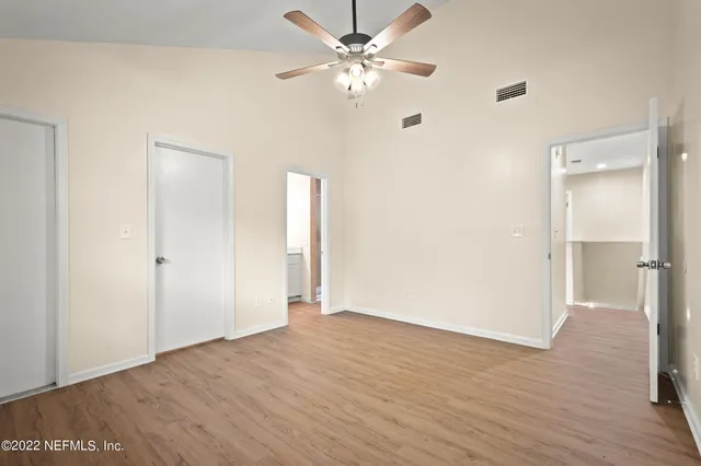 an empty room with wooden floor fan and windows