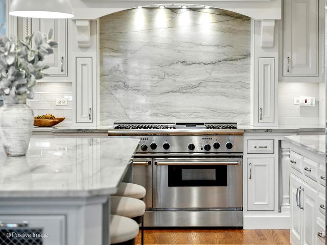 a kitchen with stainless steel appliances granite countertop a stove a sink a refrigerator and white cabinets with wooden floor