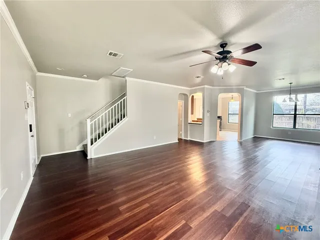 a view of an empty room with a kitchen and a ceiling fan
