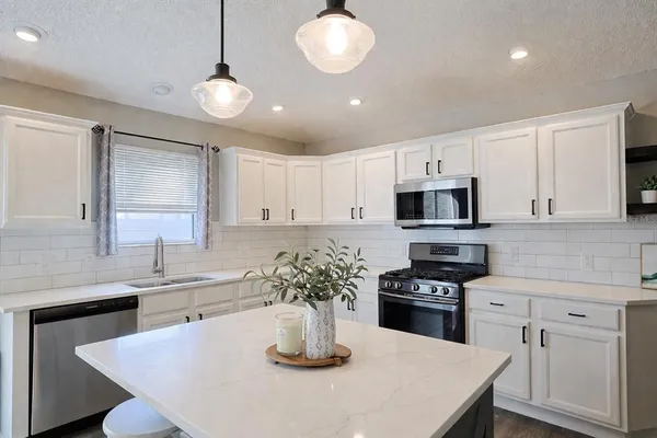 a kitchen with stainless steel appliances a kitchen island hardwood floor sink stove and white cabinets