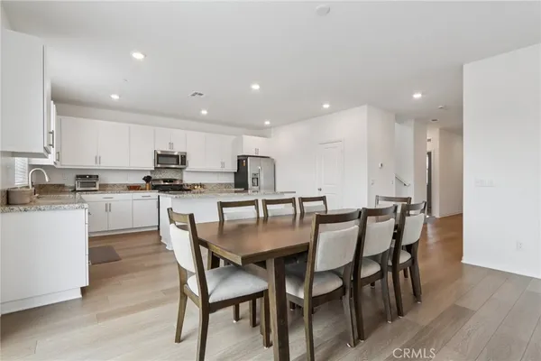 a kitchen with stainless steel appliances kitchen island granite countertop a dining table chairs and white cabinets