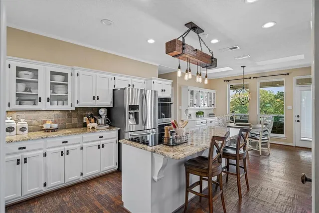 a kitchen with stainless steel appliances kitchen island granite countertop a stove a refrigerator a dining table and chairs with wooden floor