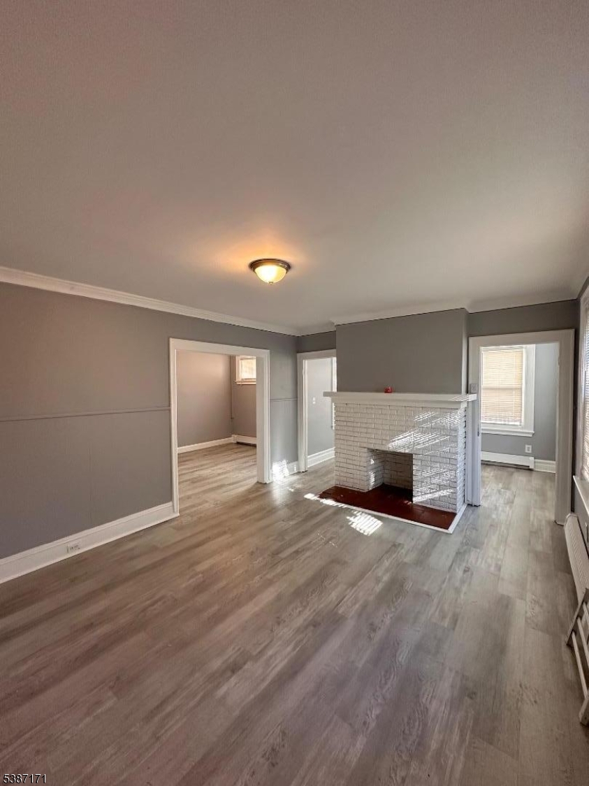 87 Lyons Avenue Newark, NJ 07112 - Photo 5 of 13 an empty room with wooden floor fireplace and windows