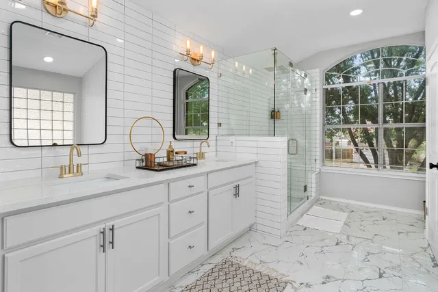 a bathroom with double vanity sink a mirror a glass door a shower and vanity