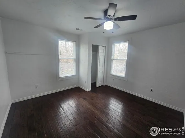 an empty room with wooden floor chandelier fan and windows