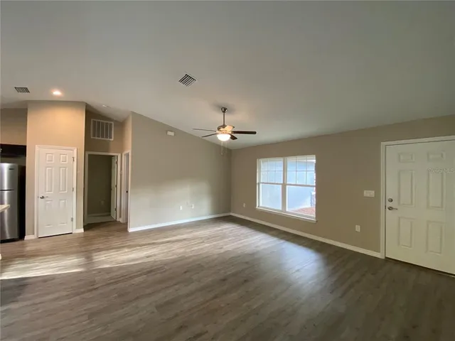 an empty room with wooden floor chandelier fan and windows