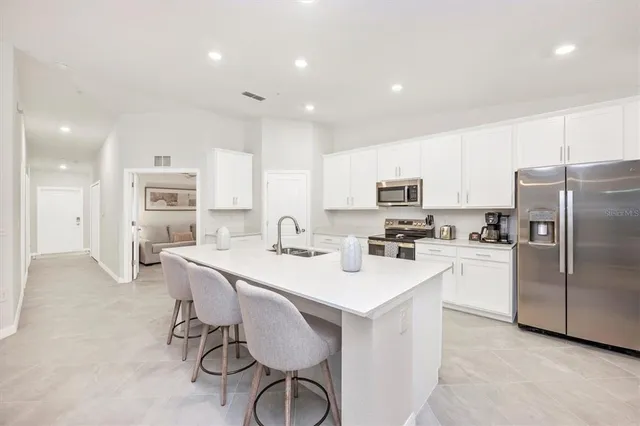 a kitchen with stainless steel appliances kitchen island granite countertop a sink dishwasher a stove a kitchen island with chairs and white cabinets