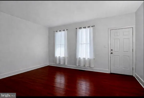 an empty room with wooden floor and windows with curtains