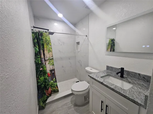 a bathroom with a granite countertop sink a toilet a mirror and shower