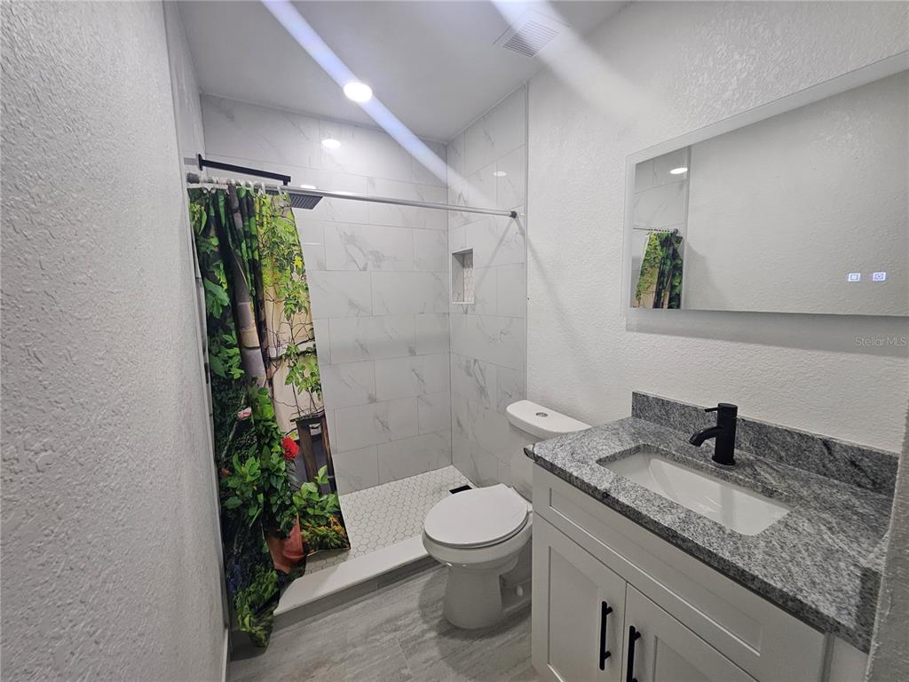5802 Mohr Loop, Unit 5802 5804 5806 5808 Tampa, FL 33615 - Photo 29 of 40 a bathroom with a granite countertop sink a toilet a mirror and shower
