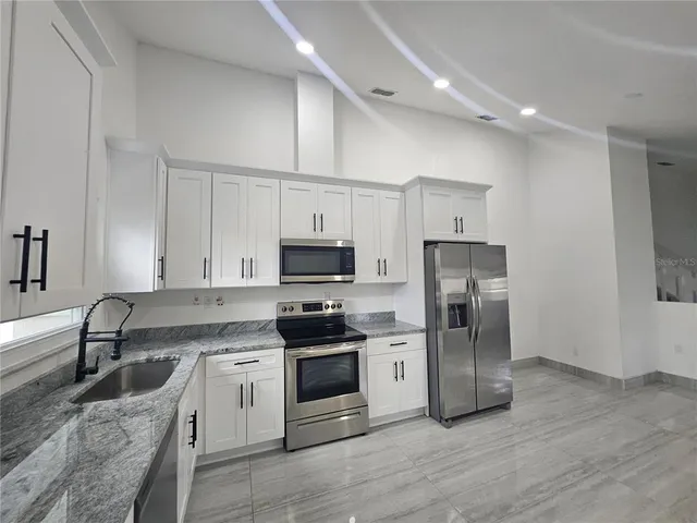 a kitchen with stainless steel appliances granite countertop a refrigerator stove a sink and white cabinets