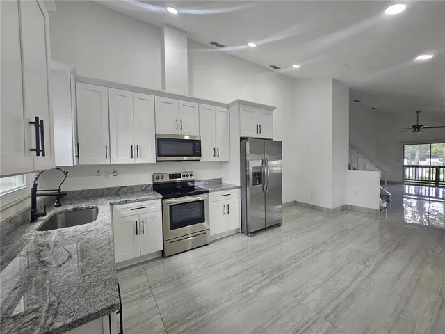 a kitchen with granite countertop a refrigerator a stove top oven a sink dishwasher and white cabinets with wooden floor