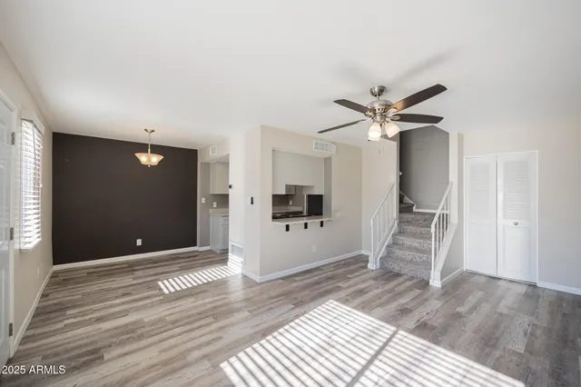 a view of an empty room with wooden floor and a ceiling fan