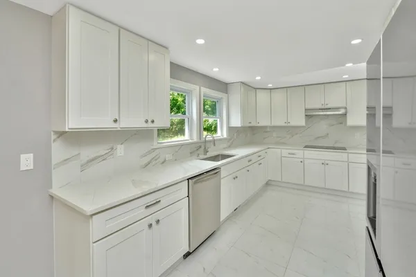 a kitchen with white cabinets appliances a sink and a window