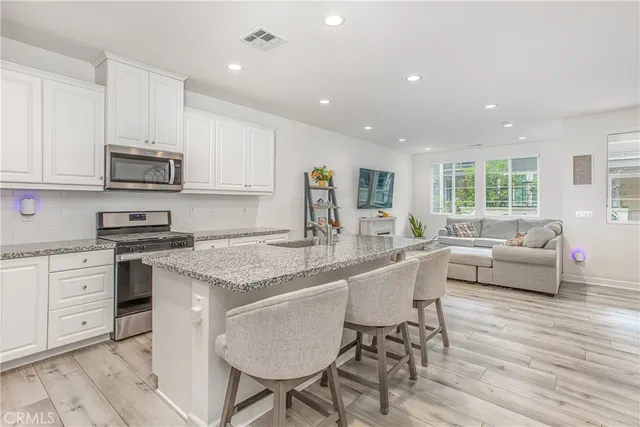 a kitchen with stainless steel appliances granite countertop a stove top oven a sink dishwasher a dining table and chairs with wooden floor