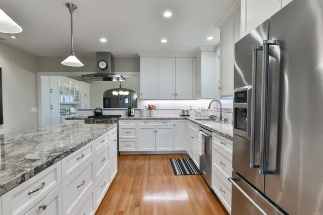 a kitchen with stainless steel appliances granite countertop a refrigerator a oven and white cabinets with granite countertops