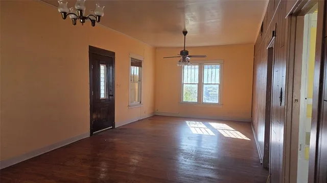 an empty room with wooden floor chandelier and windows