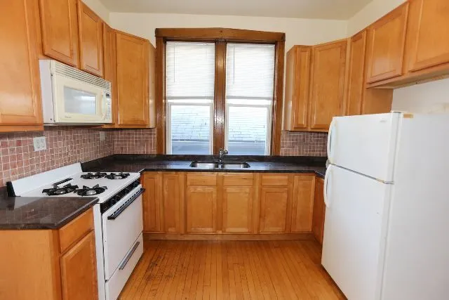 a kitchen with granite countertop a refrigerator a sink a stove and wooden cabinets