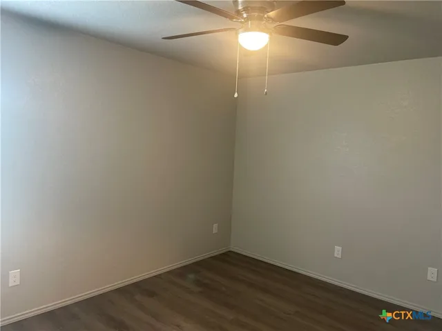 an empty room with a chandelier fan and wooden floor