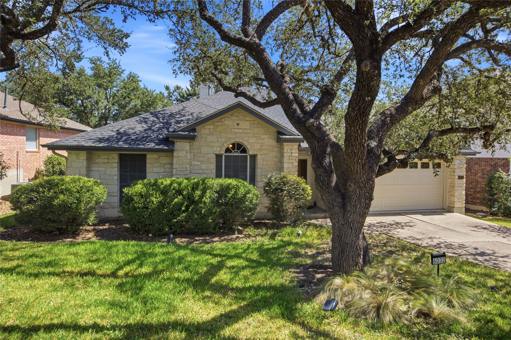 6032 Roxbury Lane Austin, TX 78739 - Photo 1 of 34 Mature shade trees frame a classic stone exterior with a neat driveway and garage.