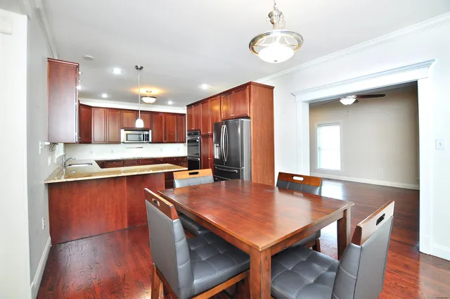 a kitchen with stainless steel appliances granite countertop a sink dishwasher a stove refrigerator and a dining table with wooden floor