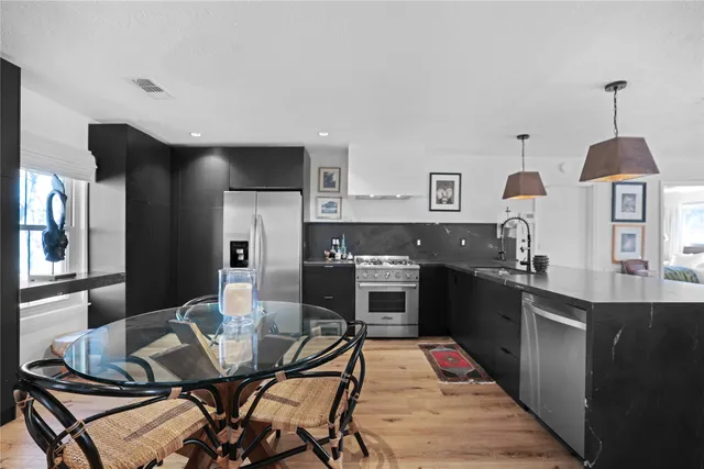 a kitchen with stainless steel appliances granite countertop a stove a sink dishwasher a dining table and chairs with wooden floor