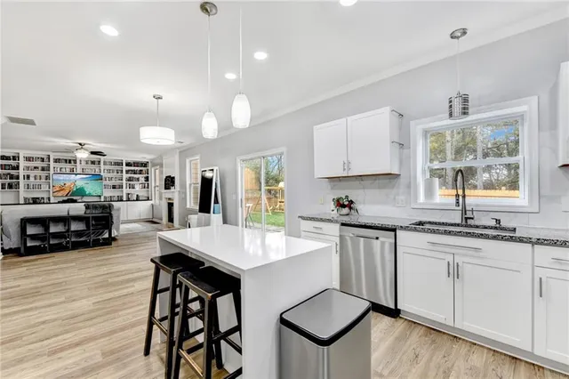 a open kitchen with stainless steel appliances granite countertop a stove a sink a refrigerator and white cabinets with wooden floor