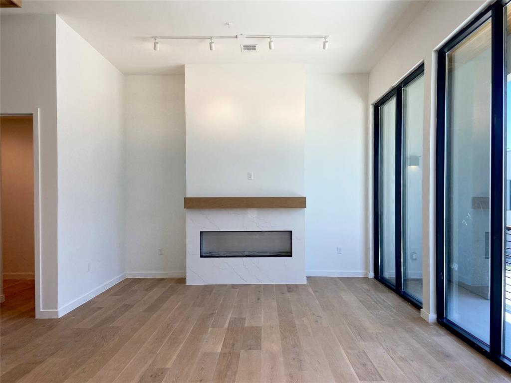 1111 Raiford Road, Unit 128 Carrollton, TX 75007 - Photo 10 of 18 Spacious living area featuring white oak wood flooring, a contemporary gas fireplace, and expansive floor-to-ceiling glass doors that open onto a balcony. (construction photos - professional photos upon completion)