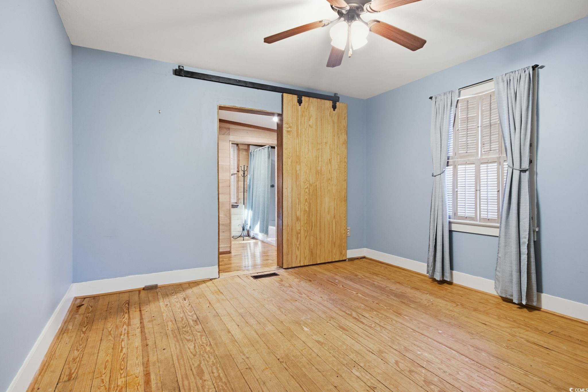 2206 Beck Street Georgetown, SC 29440 - Photo 18 of 36 Unfurnished bedroom featuring light wood-type flooring, a barn door, and ceiling fan