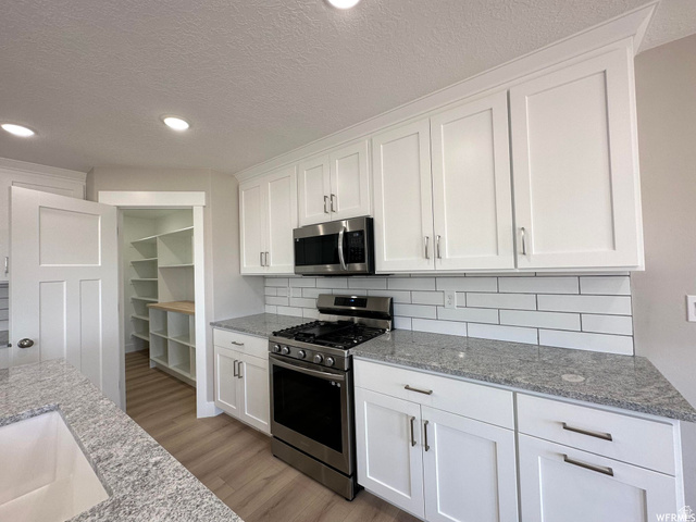 1171 West 2330 North Helper, UT 84526 - Photo 6 of 26 Kitchen featuring stainless steel appliances, white cabinets, light stone counters, light wood finished floors, and decorative backsplash