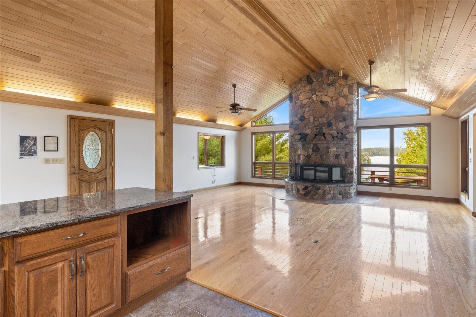 2375 Viste Point Road Ely, MN 55731 - Photo 21 of 83 Unfurnished living room with wooden ceiling with exposed beams, light wood floors, stone fireplace, high vaulted ceiling, and ceiling fan