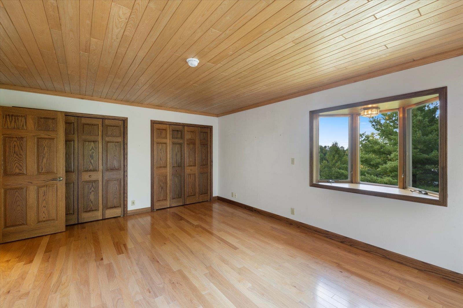2375 Viste Point Road Ely, MN 55731 - Photo 25 of 83 Primary bedroom featuring multiple closets, light wood flooring, and wooden ceiling. Bedroom is located on the lake side of the home.