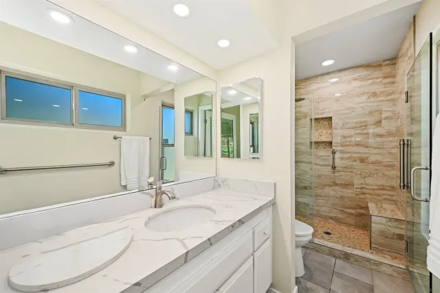a bathroom with a granite countertop sink a toilet a mirror and shower