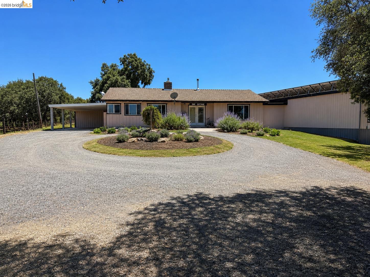 Ranch-style residence featuring a gravel circular driveway, attached carport, and a separate large structure with solar panels