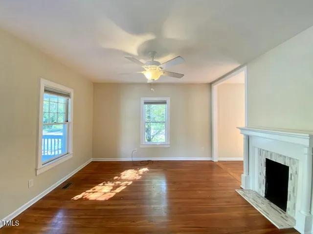 a view of an empty room with wooden floor fireplace and a window