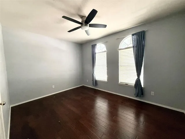 an empty room with wooden floor fan and windows