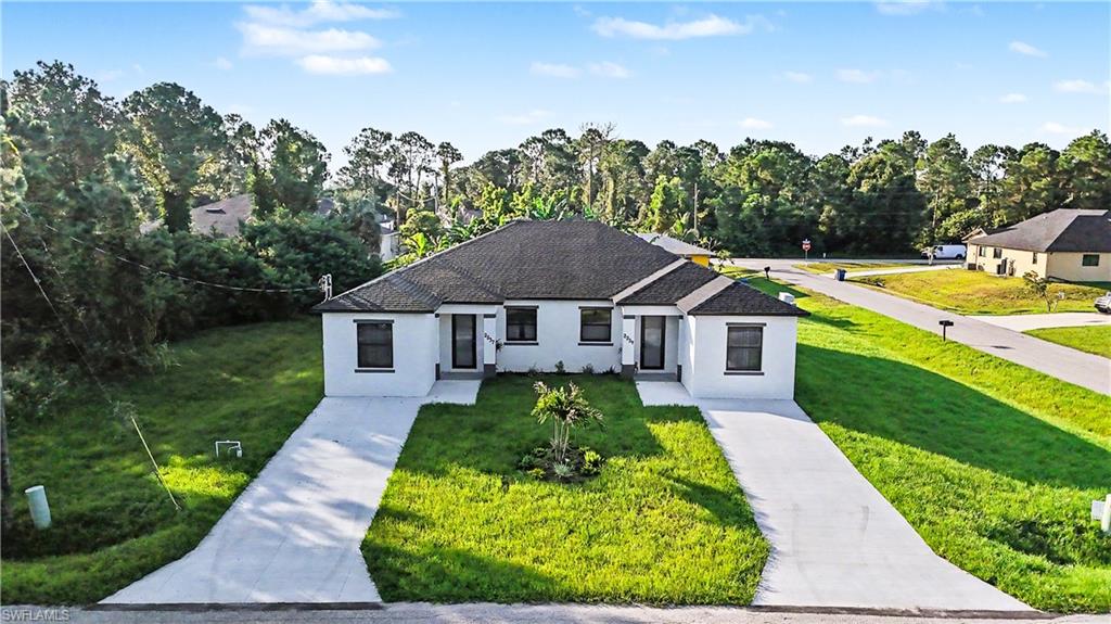 2239 Armour Road Lehigh Acres, FL 33973 - Photo 3 of 24 Duplex property featuring a white stucco exterior with black-framed windows, individual concrete driveways, and a central landscaped area with a small palm tree