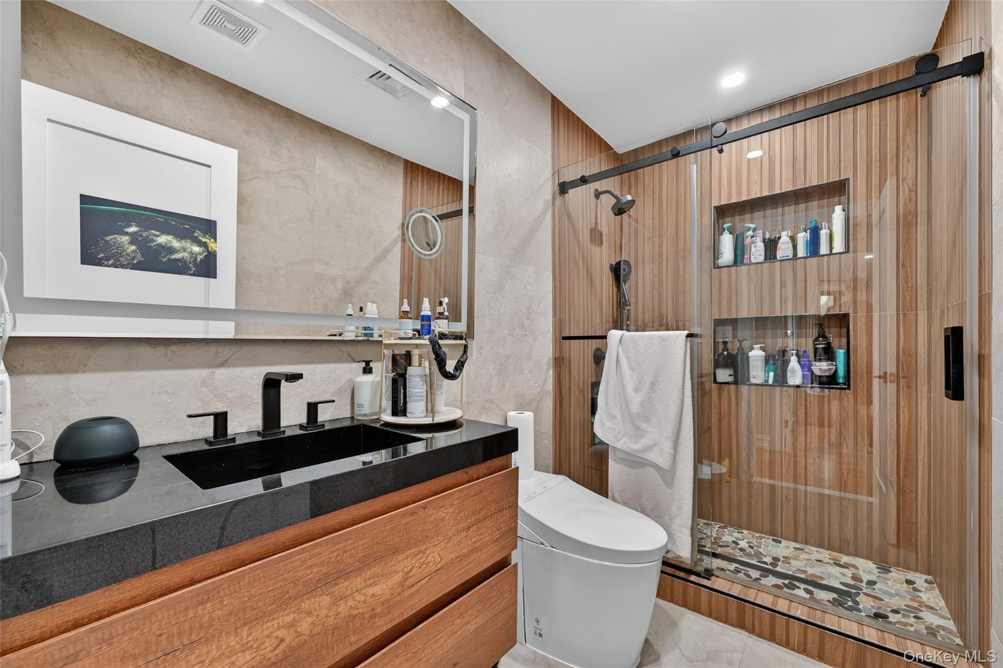 65 Wildway Bronxville, NY 10708 - Photo 28 of 42 Bathroom featuring a wood-finish vanity with a black countertop and integrated sink, a large wall-mounted mirror, and a glass-enclosed shower