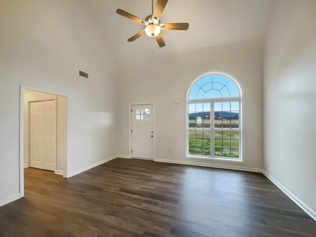 an empty room with wooden floor chandelier fan and windows