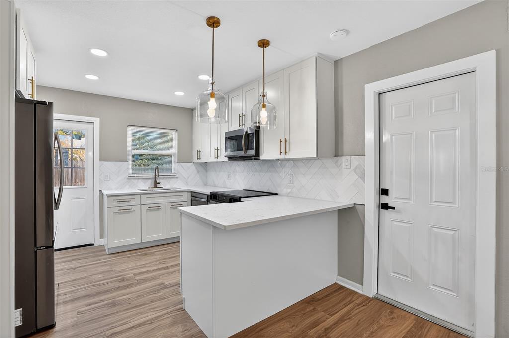 8244 125th Street Seminole, FL 33776 - Photo 6 of 32 a kitchen with kitchen island a sink dishwasher a refrigerator and white cabinets with wooden floor