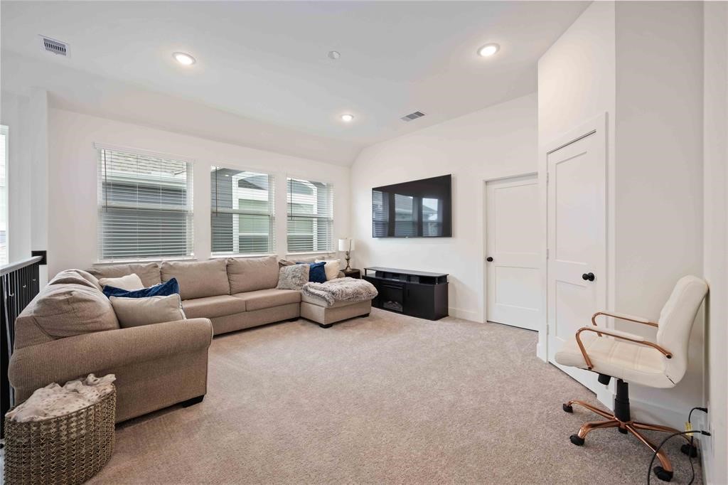 10014 Nectar Path Iowa Colony, TX 77583 - Photo 14 of 26 This spacious, bright living area features a cozy sectional sofa, a wall-mounted TV, and plush carpeting. Large windows offer ample natural light, while the neutral color palette creates a welcoming atmosphere.