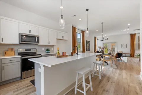 a view of a kitchen with kitchen island a dining table chairs stainless steel appliances and wooden floor