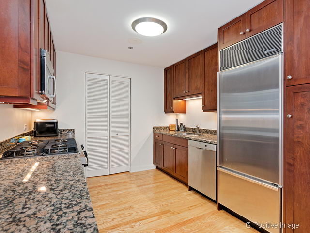60 East Monroe Street, Unit 1906 Chicago, IL 60603 - Photo 11 of 20 a kitchen with stainless steel appliances granite countertop a refrigerator a stove and a sink with wooden floor