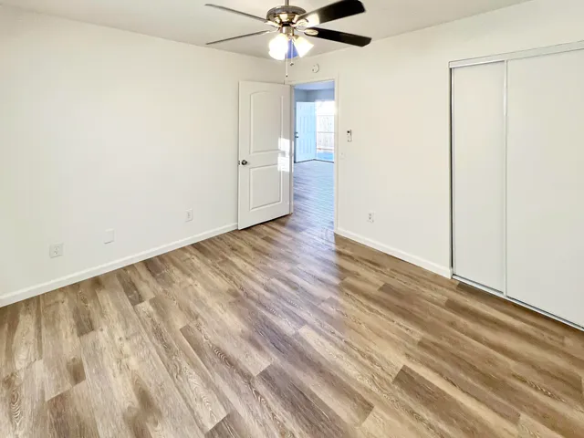 an empty room with wooden floor fan and windows