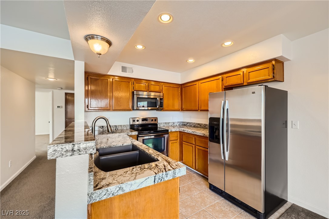 1575 West Warm Springs Road, Unit 1613 Henderson, NV 89014 - Photo 15 of 39 Kitchen featuring brown cabinetry, a peninsula, a sink, and appliances with stainless steel finishes