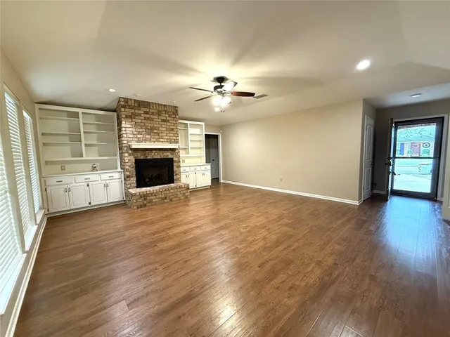 an empty room with fireplace wooden floor and chandelier fan