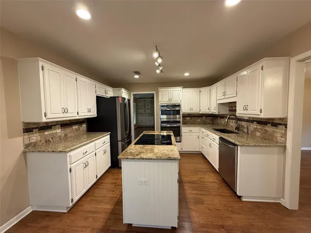 a large kitchen with stainless steel appliances kitchen island granite countertop a stove a sink dishwasher and a refrigerator with wooden floor