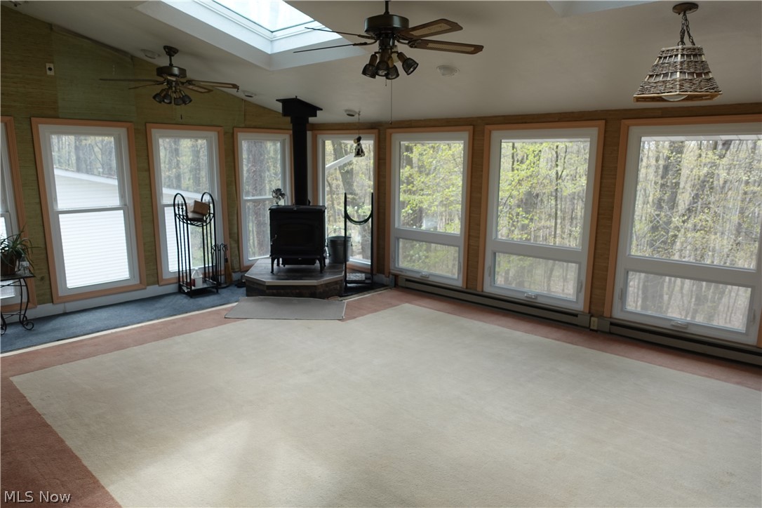 15488 Hatfield Road Rittman, OH 44270 - Photo 18 of 36 Unfurnished living room with lofted ceiling with skylight, ceiling fan, carpet, baseboard heating, and a wood stove